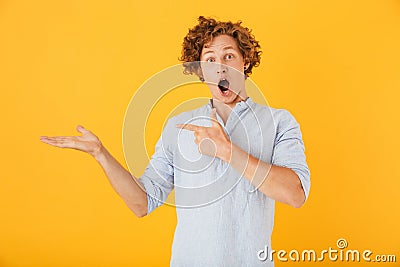 Photo of shocked european man 20s shouting and holding copyspace at palm, isolated over yellow background Stock Photo