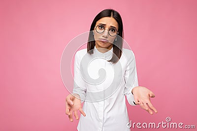 Photo shot of beautiful sorrowful young brunette woman wearing white shirt and stylish optical glasses isolated over Stock Photo