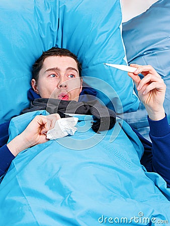 Photo of sick brunet man in scarf with thermometer in hand lying in bed. Stock Photo