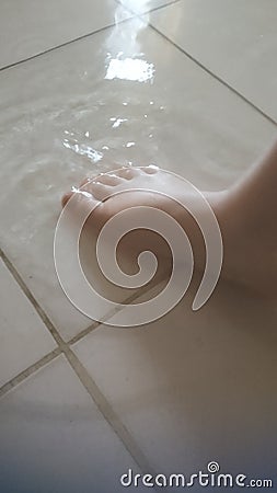 a photo of a small child& x27;s feet submerged in a very shallow puddle of water during the day Stock Photo