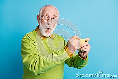 Photo of surprised grandfather hold telephone amazed face wear eyeglasses green sweater isolated blue color background Stock Photo