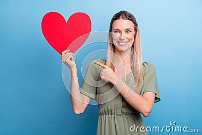 Photo of sweet shiny young woman dressed green clothes pointing finger large red heart card empty space smiling isolated Stock Photo