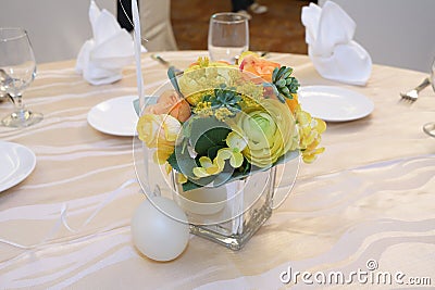 A pot of artificial flowers set up as decoration on a dinning table with light colored beige table cloth Stock Photo