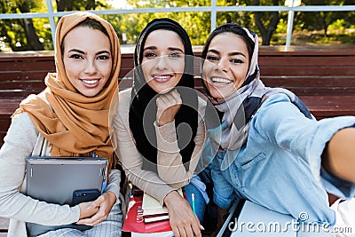 Photo of three muslim female students wearing headscarfs sitting on bench in park Stock Photo