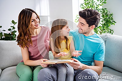 Photo of three people sit couch little kid read book story tell her parents mommy daddy in house indoors Stock Photo