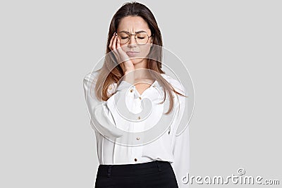 Photo of tired overworked female office worker keeps eyes closed, feels sleepy, holds hand on cheek, dressed in stylish clothes, i Stock Photo