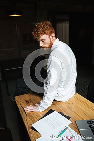 Photo of tired readhead curly bearded man, sitting on wooden tab Stock Photo