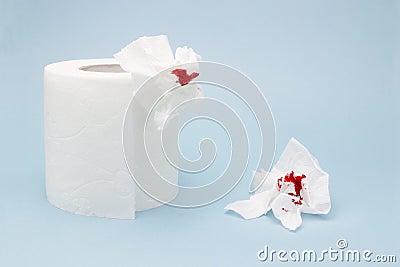 A photo of a toilet paper roll and two used bloody toilet paper sheets. Blood drops and traces. Menstrual or hemorrhoids bleeding. Stock Photo