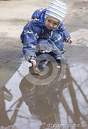 A 2 -year-old boy playing with a leaf in a puddle Stock Photo