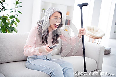 Photo of unhappy angry old woman hold hand cane stick switch channel scream tv indoors inside house home Stock Photo