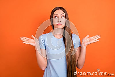 Photo of unsure brown hairdo young lady shrug shoulders look empty space wear blue t-shirt isolated on vivid orange Stock Photo