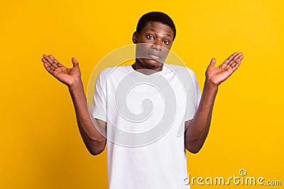 Photo of unsure brunet young guy shrug shoulders wear white t-shirt isolated on yellow color background Stock Photo
