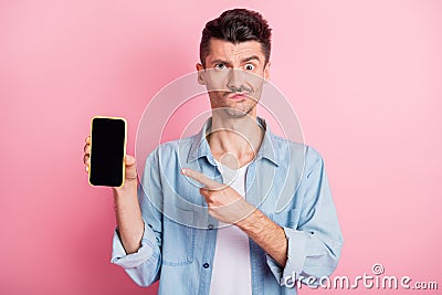 Photo of upset young brunette man point finger index screen phone feedback isolated on pink color background Stock Photo