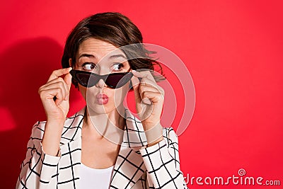 Photo of young attractive girl curious look empty space pouted lips hands touch sunglasses isolated over red color Stock Photo