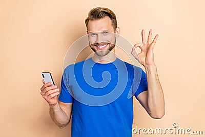Photo of young guy use mobile show fingers okey symbol recommend promo perfect isolated over beige color background Stock Photo