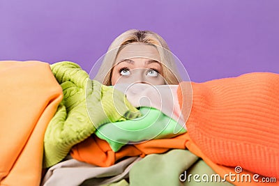 Photo of young lady hide face behind big pile stack clothes look up empty space isolated on violet color background Stock Photo