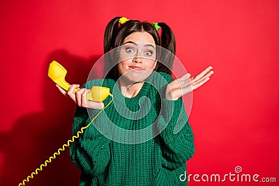 Photo of young unsure uncertain puzzled woman hold yellow telephone shrugging shoulders isolated on red color background Stock Photo