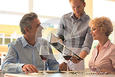 Young waiter showing menu to mature couple at restaurant Stock Photo