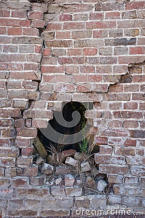 Photograph of a broken porous old ruined brick wall with hole after accident, many cracks, collapse hazard, dark background Stock Photo