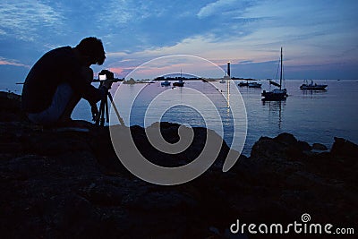 Photographer capturing the beautiful view of the boats in the sea and the lighthouse Stock Photo