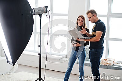 Photographer explaining about the shot to his assistant in the studio and looking on laptop. Teamwork and brainstorm Stock Photo
