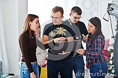 Photographer explaining about the shot to his team in the studio and looking on laptop. Talking to his assistants holding a camera Stock Photo