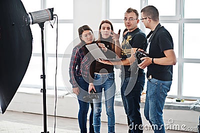 Photographer explaining about the shot to his team in the studio and looking on laptop. Talking to his assistants holding a camera Stock Photo