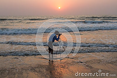 The photographer photographs from a tripod standing in the sea. India, Karnataka, Gokarna, February 2017 Editorial Stock Photo