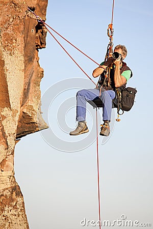 Photographer and rock climber taking pictures in while hanging in front of a rock Stock Photo
