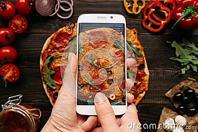 Photographing food. Hands taking picture of delisious pizza with smartphone Stock Photo