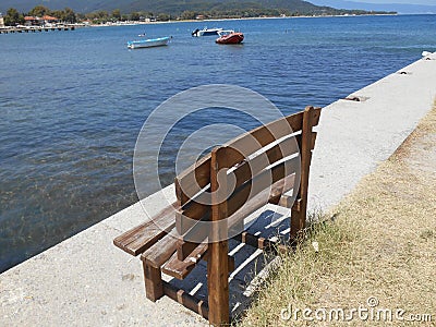 Brown bench with sea, boats, mountain and beach in background, Olimpiada, Greece Editorial Stock Photo