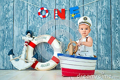 Photoshoot for a boy of one year. Little sea captain, sailor on toy ship with steering wheel. Sea anchor and lifebuoy on gray Stock Photo