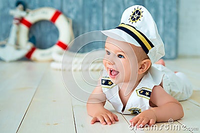 Photoshoot for a boy of one year. Little sea captain, sailor on toy ship with steering wheel. Sea anchor and lifebuoy on gray Stock Photo