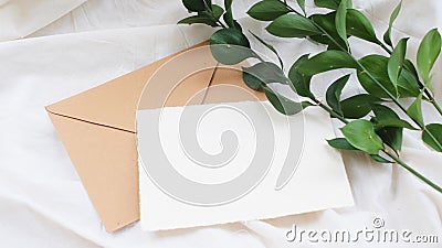 Photostock wedding styled composition. Feminine envelope mockup scene with ruscus leaves, silk ribbon, blank greeting card, on cre Stock Photo