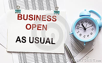 The phrase Business as usual printed on a notebook. Documents, alarm clock and pen lie on a white background Stock Photo