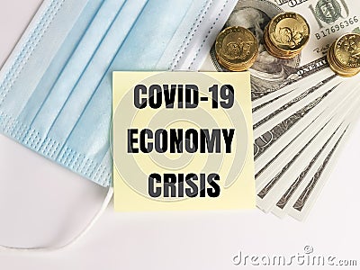 Phrase COVID-19 ECONOMY CRISIS on note book with dollar bank notes, coins and face mask. Stock Photo