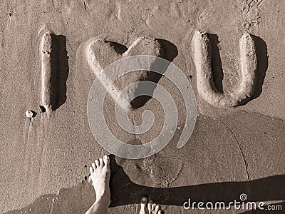 Phrase `I love you` made of sand. Bulky sandy letters with woman feet and wave. Black and white. Stock Photo