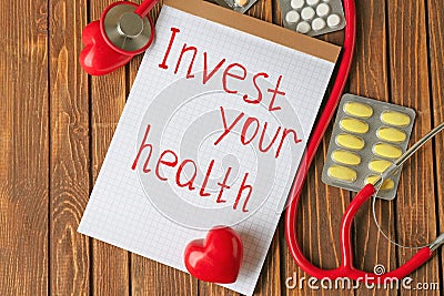 Phrase Invest your health written on sheet of paper, stethoscope and pills on wooden background Stock Photo