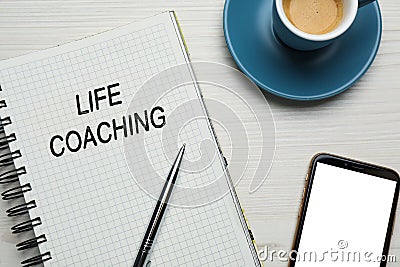 Phrase Life Coaching written in notebook, pen, smartphone and cup coffee on white wooden table, flat lay Stock Photo