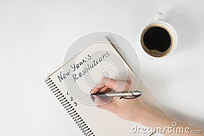 Phrase New Year`s resolutions in the notebook. Female hand with pen and cup of coffee Stock Photo