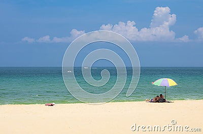 Happy couple men under colourful umbrella are resting on the beautiful tropical beach at Phuket Stock Photo