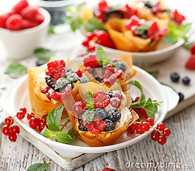 Phyllo pastry fruit cups with whipped cream filling topped with mix fresh berries sprinkled with powder sugar on a white plate clo Stock Photo