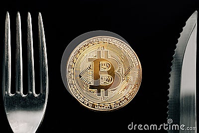 Physical Golden Crytocurrency Coin between fork and knive. Stock Photo