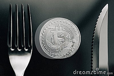 Physical silver Crytocurrency Coin between fork and knive. Stock Photo