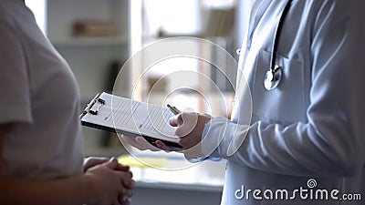 Physician listening female patient complaints and writing down in medical form Stock Photo