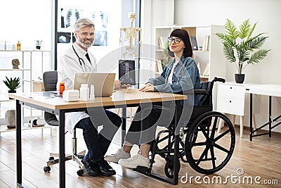 Physician with tablet sitting near lady with disability Stock Photo