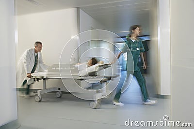 Physicians Moving Patient On Gurney Through Hospital Corridor Stock Photo