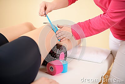 Physiotherapist applying kinesio tape on female patient`s knee. Close up cropped shot. Kinesiology, physical therapy. Stock Photo