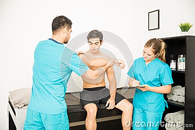 Physiotherapist Examining Shirtless Customer`s Hand While Cowork Stock Photo