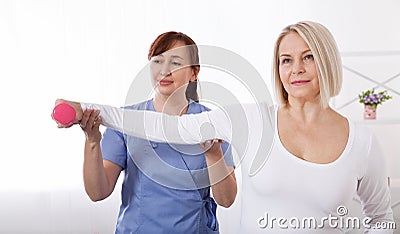 A physiotherapist helps an older woman recover from an injury through exercise with dumbbells. Stock Photo
